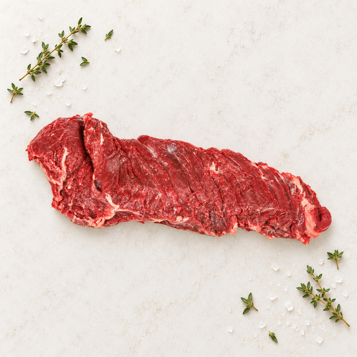 Raw skirt steak on light stone with thyme and sea salt.