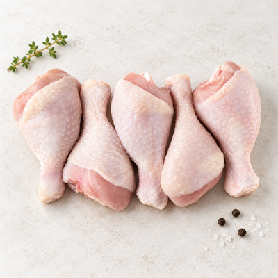 Five raw skin-on chicken drumsticks on a light stone surface, with thyme at the upper left and sea salt and black peppercorns at the lower right.
