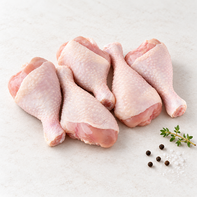 Five raw skin-on chicken drumsticks on a light stone surface with thyme, sea salt and black peppercorns.