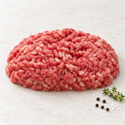Raw ground lamb in a rounded mound on a light stone surface with thyme, sea salt and black peppercorns.
