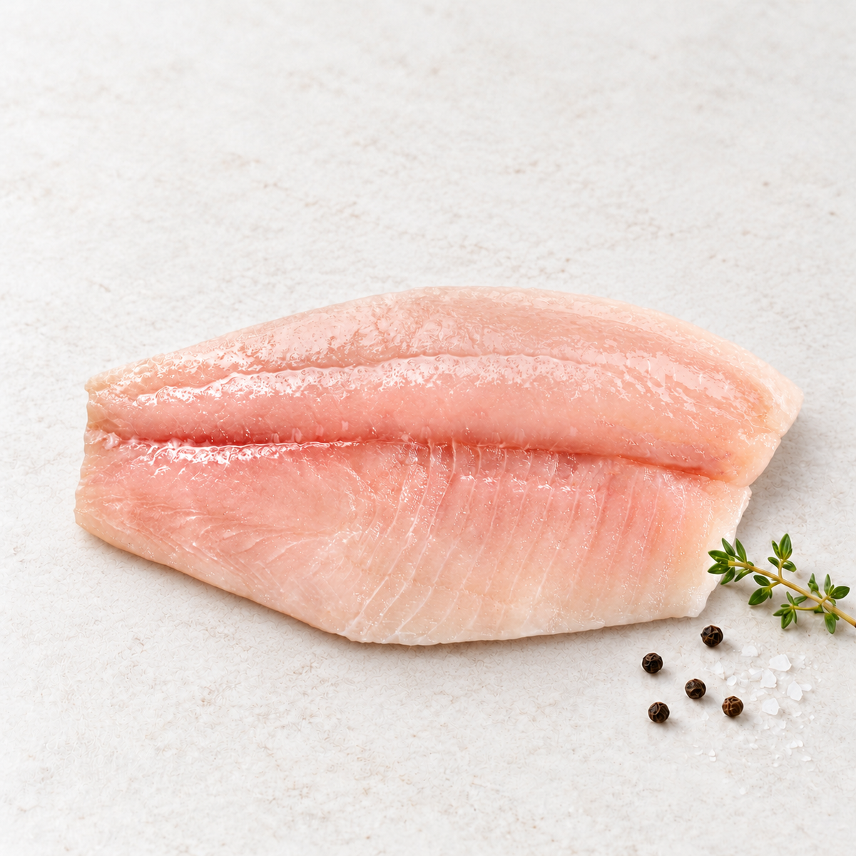 Raw red snapper fillet on a light stone surface with thyme, sea salt and peppercorns