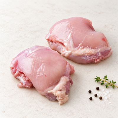 Two raw boneless, skinless chicken thighs on a light stone surface with thyme, sea salt and black peppercorns.
