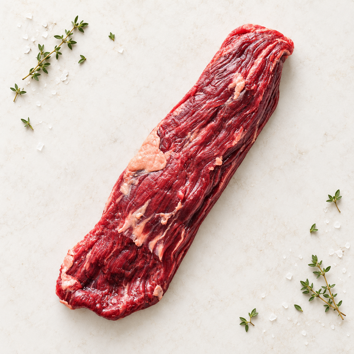 Raw Wagyu skirt steak on light stone with thyme and sea salt.